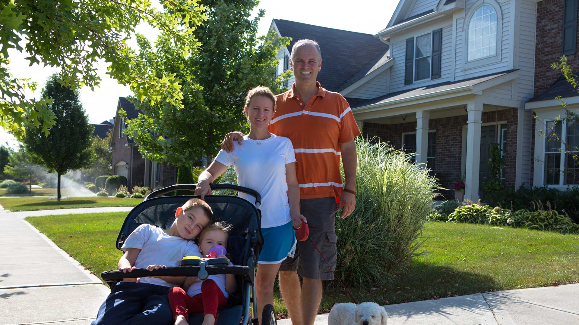 A smiling family walking their kids and dog